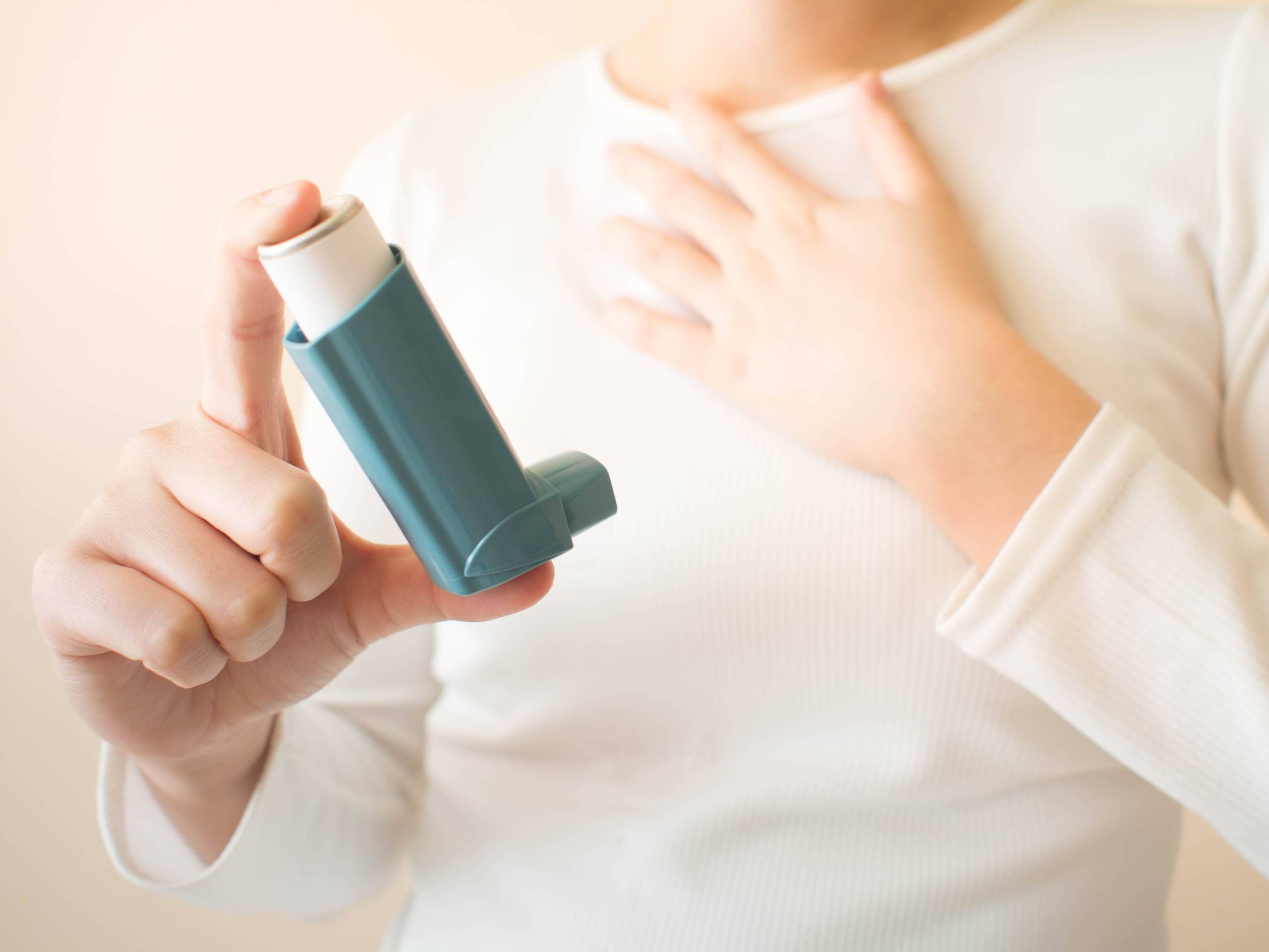 Young female in white t-shirt using blue asthma inhaler for relief asthma attack. SpeedGreens.
