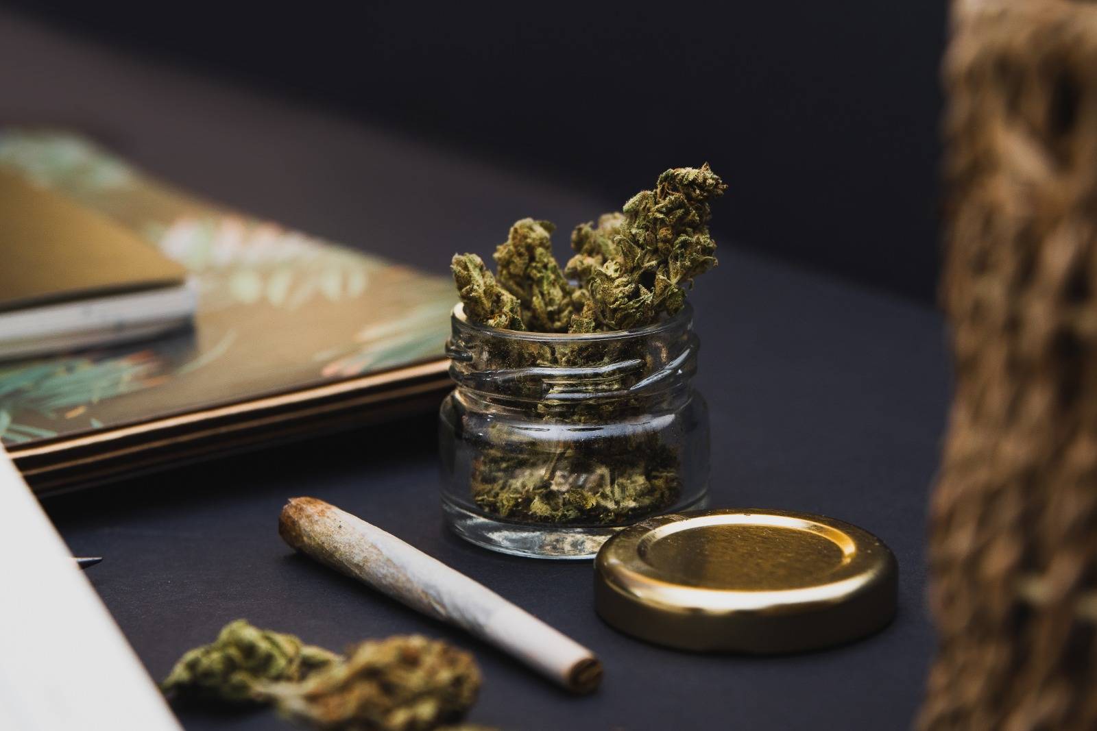 Jar of cannabis Ontario buds, gold lid, notebooks, joint on black background. Speed Greens.